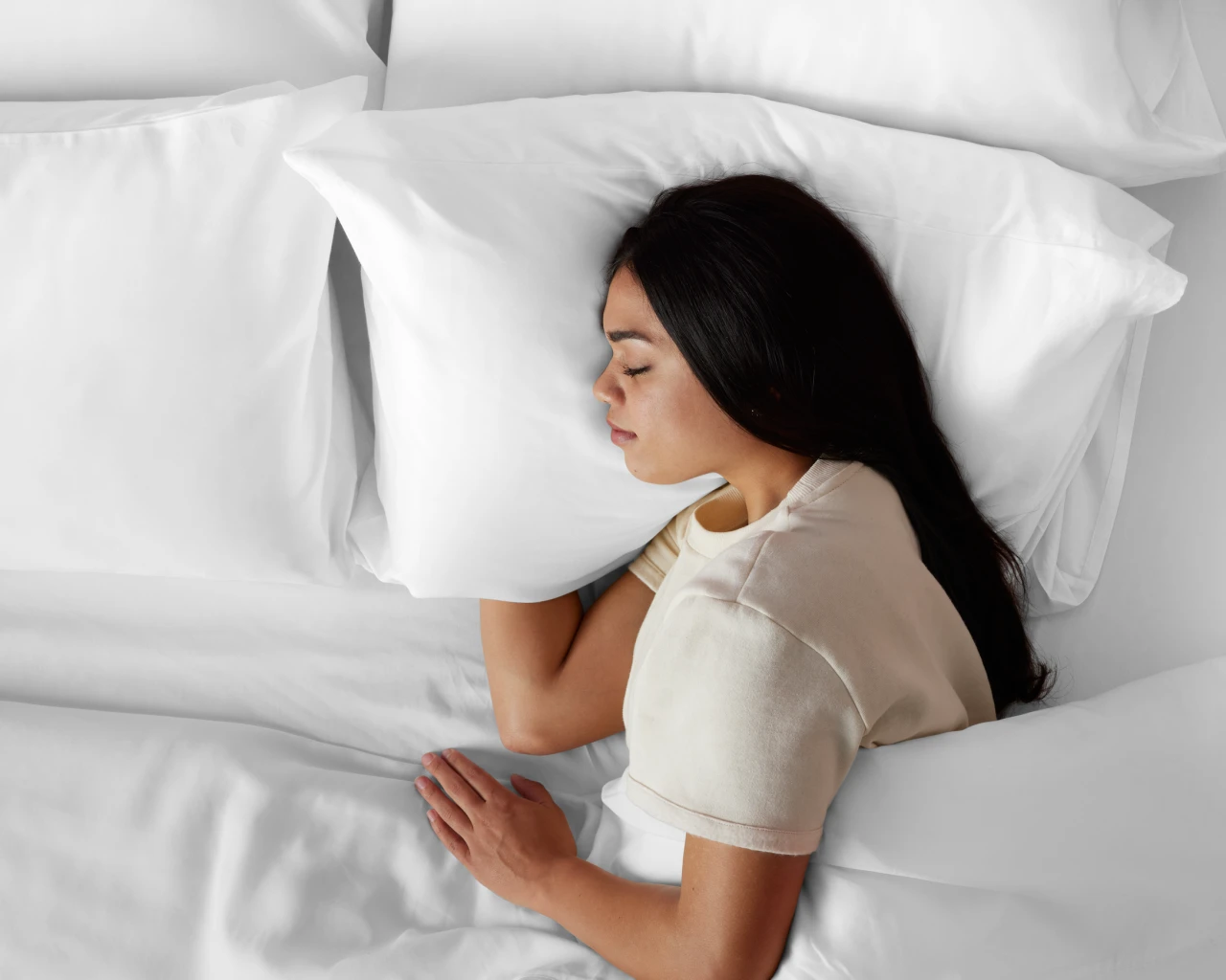 A woman lies on her side in bed, hugging a white pillow and sleeping peacefully in a simple and comfortable environment.