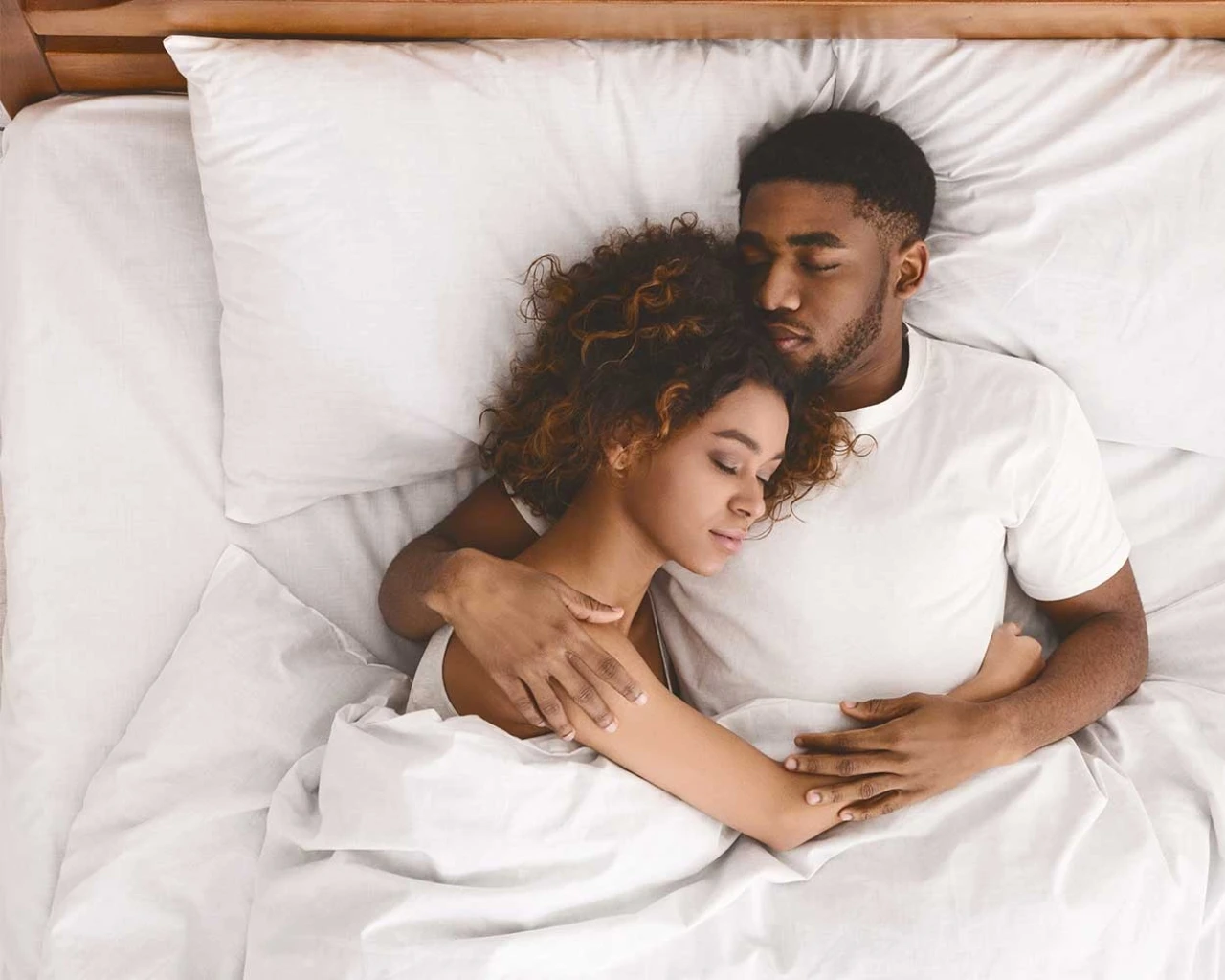 A couple is sleeping peacefully in each other's arms on a white bed, a scene of warmth and tranquility.