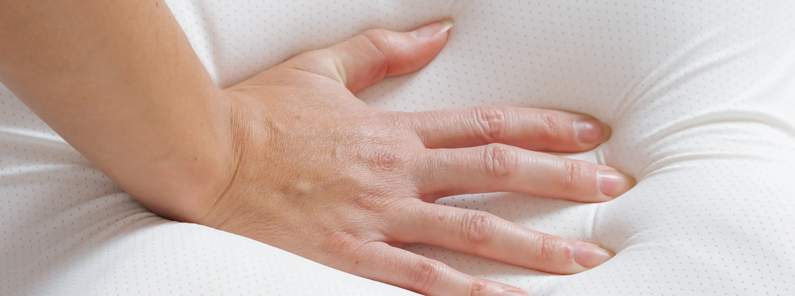"A close-up of a hand gently pressing into a soft pillow, showcasing its plush texture.